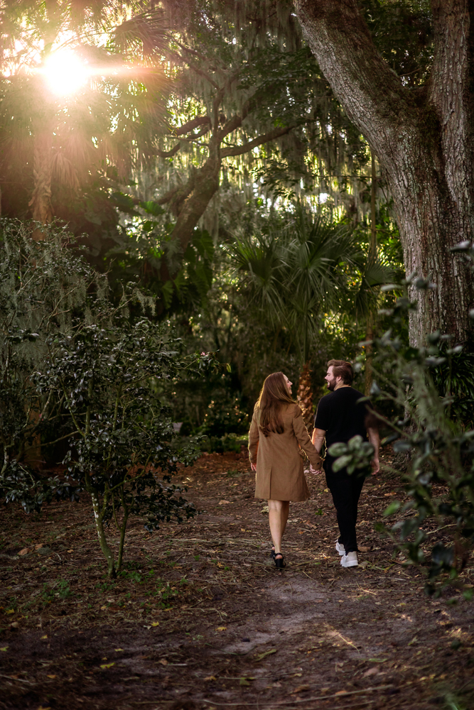 Thomas and Emily walking hand in hand through the lush gardens at Leu Gardens during their engagement session with Orlando Florida photographer Natalie Szolomayer