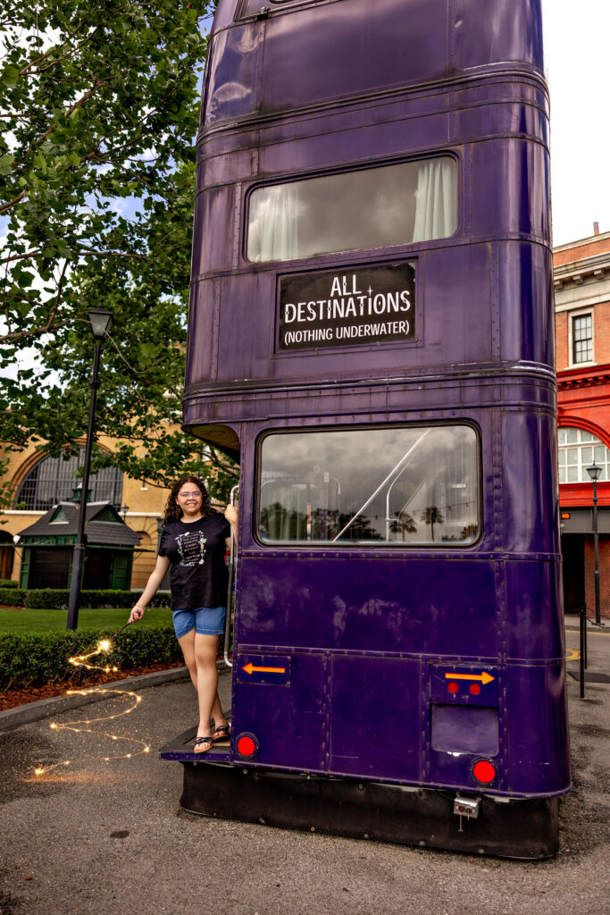 Haleigh smiling next to the purple Knight Bus at Universal Orlando, holding a sparkling wand during her fun senior session photos.