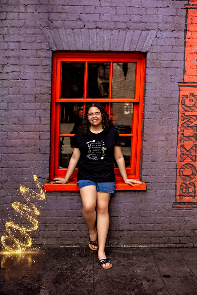"Haleigh smiling by a red window in Diagon Alley at Universal Orlando, holding a sparkling wand during her fun senior session photos.