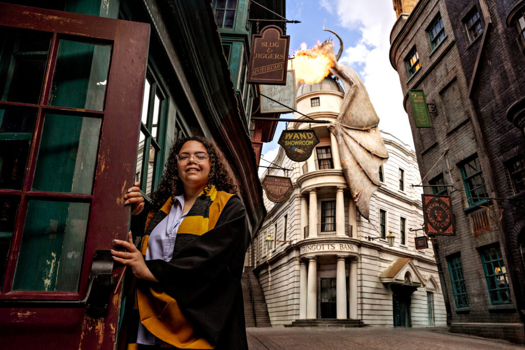 Haleigh smiling by a red door in Diagon Alley during her Universal Orlando senior session, with the fire-breathing dragon on Gringotts Bank in the background