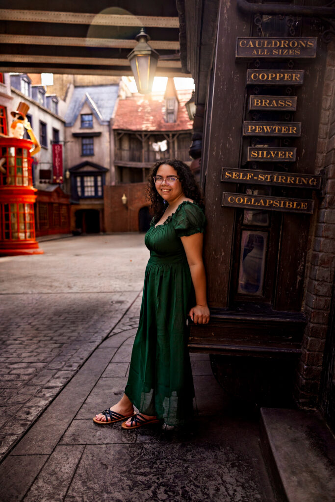 Haleigh in a green dress posing by a cauldrons shop door in Diagon Alley at Universal Orlando during her senior photography session