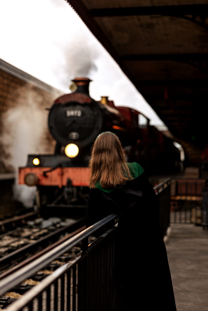 Madison in her hogwarts robe watching the train approach Hogsmeade station